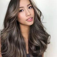 Mujer con cabello largo y ondulado con mechas balayage en tonos castaños y rubios cenizos, luciendo un estilo natural y moderno.