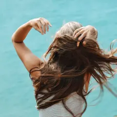 Mujer con cabello largo y castaño, jugando con su pelo. Una forma natural de como disimular las canas es con peinados que aporten volumen.