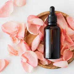 Frasco de aceites esenciales despigmentantes rodeado de pétalos de rosa.