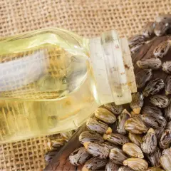 Aceite de ricino para manchas de la cara. Botella de aceite de ricino junto a semillas de ricino sobre fondo de arpillera.