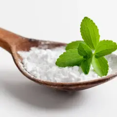 Cucharada de polvo blanco, que es la stevia, con hojas verdes frescas encima.