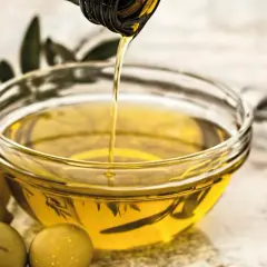 Aceite vegetal dorado se vierte en un cuenco, junto a aceitunas y utensilios de cocina.