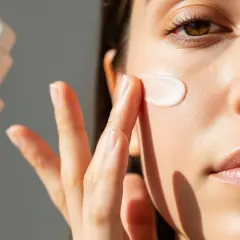 Una mano aplica crema con ácido salicílico y vitamina C en el rostro.