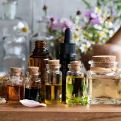 Frascos de vidrio con aceites esenciales para aromaterapia, rodeados de flores y hierbas.