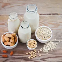 Tres botellas con diferentes tipos de leches vegetales: almendra, soja y avena, junto a sus ingredientes.