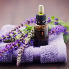Frasco de aceite esencial de salvia con flores moradas sobre toalla. Descubre las maravillosas aceite de salvia propiedades para tu bienestar.