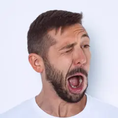 Hombre con barba y tics nerviosos musculares, guiñando un ojo y con la boca abierta en un gesto de sorpresa o grito.