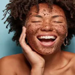 Mujer sonríe feliz con mascarilla exfoliante en el rostro. Descubre cómo exfoliar la piel para una tez radiante.