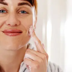 Mujer sonriente aplicándose crema con glicerina para la cara. Su piel luce hidratada y cuidada.
