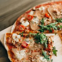 Pizza saludable para dieta, con rúcula fresca, tomates cherry y queso derretido sobre una base crujiente.