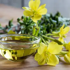 Aceite de onagra en un cuenco de cristal, rodeado de flores amarillas. Ideal para la dosis de menopausia.