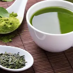 Té verde en polvo y hojas secas junto a una taza de té verde. Descubre cuál es el mejor té para adelgazar.