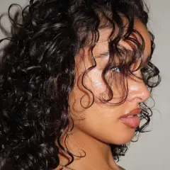 Primer plano de una mujer con una hermosa forma de pelo rizado y oscuro, con mechones cayendo sobre su rostro.