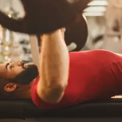 Hombre con barba haciendo press de banca. Si buscas qué hacer para engordar, el entrenamiento de fuerza es clave.