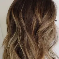 Cabello ondulado con un degradado de rubio a raíz castaña, con reflejos dorados que le dan luz.
