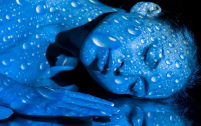 Una persona con la piel pintada de azul, cubierta de gotas blancas que parecen reflejar **que es la luz azul**.