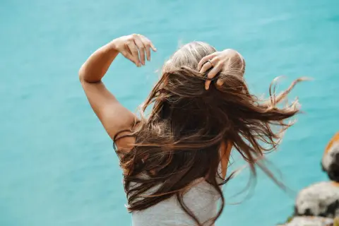 Mujer con cabello largo y castaño, jugando con su pelo. Una forma natural de como disimular las canas es con peinados que aporten volumen.
