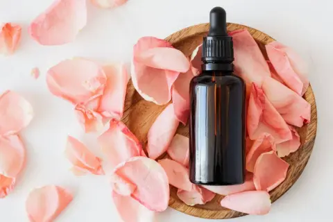 Frasco de aceites esenciales despigmentantes rodeado de pétalos de rosa.