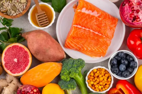 Salmón, batatas, brócoli, arándanos y semillas son algunos de los alimentos con vitamina B que se ven en la imagen.