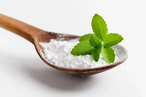 Cucharada de polvo blanco, que es la stevia, con hojas verdes frescas encima.