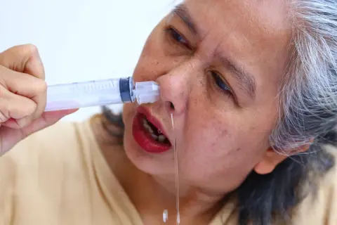 Mujer mayor se aplica suero fisiológico casero con jeringa para aliviar congestión nasal.