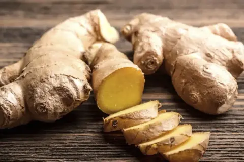Raíces de jengibre enteras y cortadas en rodajas, mostrando su interior amarillo vibrante. Un tesoro natural con innumerables propiedades del jengibre.