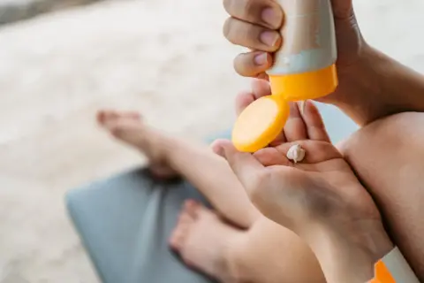 Manos aplicando crema solar en la palma. ¡Revisa la caducidad crema solar antes de usarla para proteger tu piel!