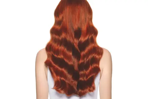 Cabello largo y ondulado con un vibrante color de pelo cobrizo dorado que brilla bajo la luz.