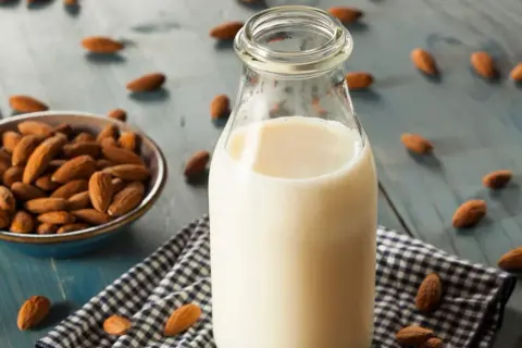 Botella de leche de almendras junto a un cuenco con almendras. Descubre las leche de almendras propiedades y beneficios.