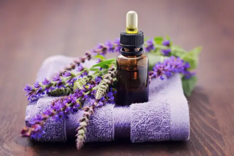 Frasco de aceite esencial de salvia con flores moradas sobre toalla. Descubre las maravillosas aceite de salvia propiedades para tu bienestar.