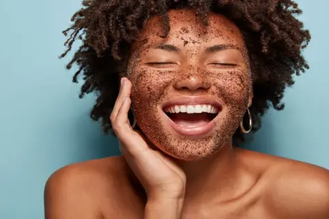 Mujer sonríe feliz con mascarilla exfoliante en el rostro. Descubre cómo exfoliar la piel para una tez radiante.
