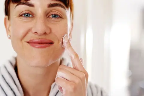 Mujer sonriente aplicándose crema con glicerina para la cara. Su piel luce hidratada y cuidada.