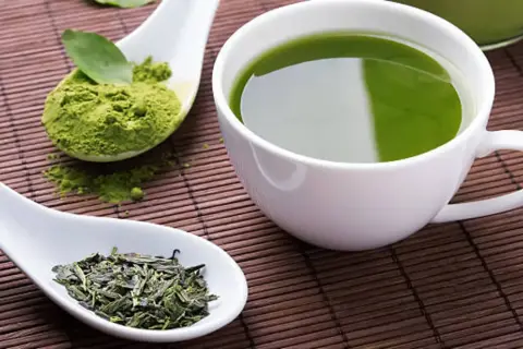 Té verde en polvo y hojas secas junto a una taza de té verde. Descubre cuál es el mejor té para adelgazar.