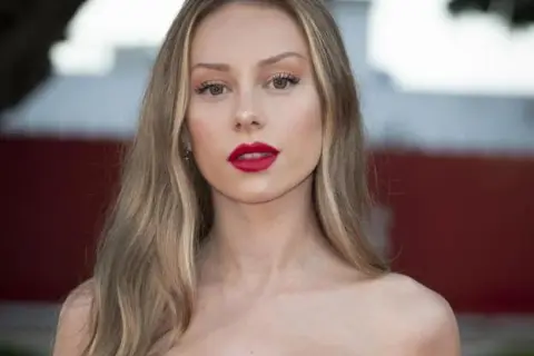 Mujer con labios rojos y cabello largo con mechas rubias naturales que brillan bajo la luz.