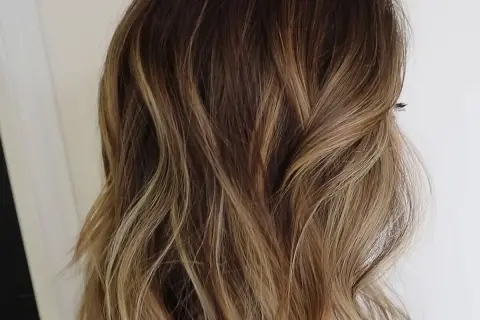 Cabello ondulado con un degradado de rubio a raíz castaña, con reflejos dorados que le dan luz.