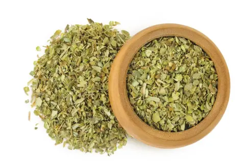 Hierbas secas de mejorana en un cuenco de madera y esparcidas. Descubre las mejorana propiedades para tu cocina y bienestar.