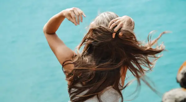 Mujer con cabello largo y castaño, jugando con su pelo. Una forma natural de como disimular las canas es con peinados que aporten volumen.