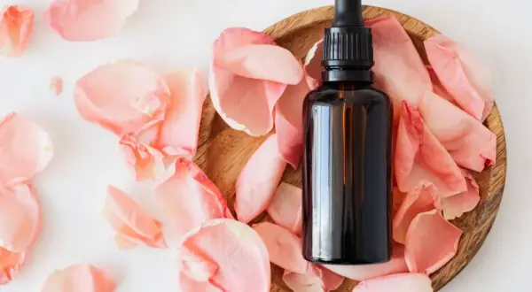 Frasco de aceites esenciales despigmentantes rodeado de pétalos de rosa.
