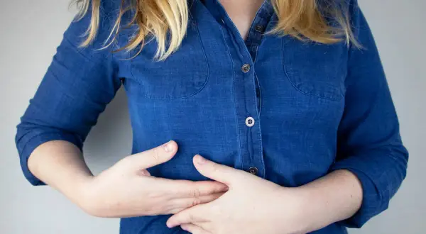 Persona con las manos en el abdomen, sintiendo pinchazos en el costado derecho debajo de las costillas.