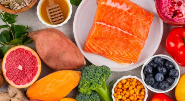 Salmón, batatas, brócoli, arándanos y semillas son algunos de los alimentos con vitamina B que se ven en la imagen.