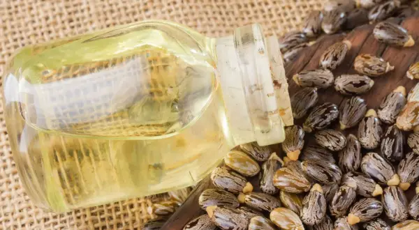 Aceite de ricino para manchas de la cara. Botella de aceite de ricino junto a semillas de ricino sobre fondo de arpillera.