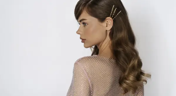 Mujer con cabello castaño con ondas al agua, adornado con pasadores dorados. Luce un vestido rosa brillante.
