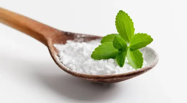 Cucharada de polvo blanco, que es la stevia, con hojas verdes frescas encima.