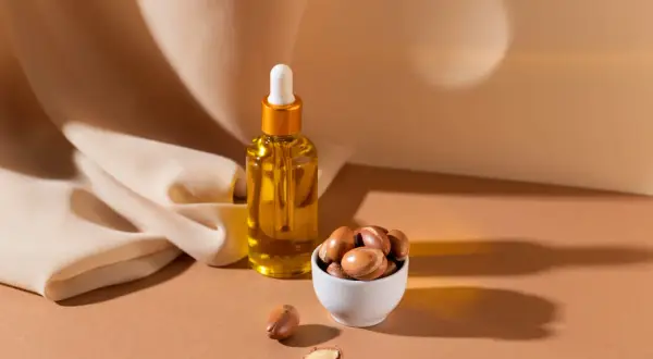 Aceite de argán en frasco y frutos secos en cuenco. Descubre las maravillosas propiedades del aceite de argán para tu piel y cabello.
