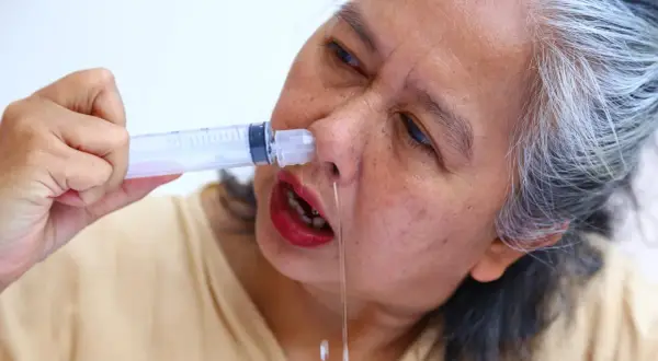Mujer mayor se aplica suero fisiológico casero con jeringa para aliviar congestión nasal.
