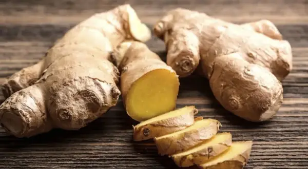 Raíces de jengibre enteras y cortadas en rodajas, mostrando su interior amarillo vibrante. Un tesoro natural con innumerables propiedades del jengibre.