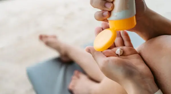 Manos aplicando crema solar en la palma. ¡Revisa la caducidad crema solar antes de usarla para proteger tu piel!