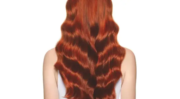 Cabello largo y ondulado con un vibrante color de pelo cobrizo dorado que brilla bajo la luz.
