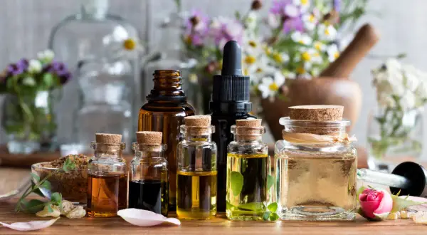 Frascos de vidrio con aceites esenciales para aromaterapia, rodeados de flores y hierbas.