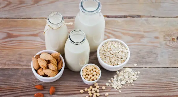 Tres botellas con diferentes tipos de leches vegetales: almendra, soja y avena, junto a sus ingredientes.